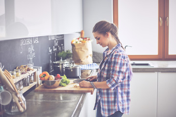 Obraz na płótnie Canvas Young woman cutting vegetables in kitchen near desk