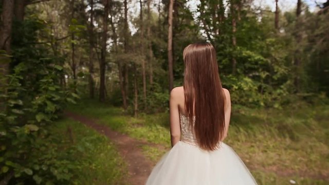 Gorgeous stylish bride in a vintage white dress, walking in the forest. Rear view.