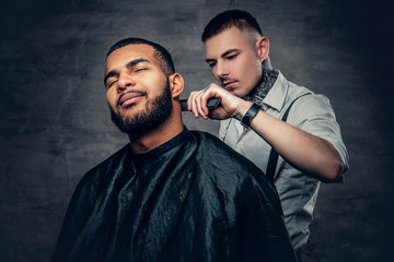 Tattooed barber makes haircut to a Black bearded male.