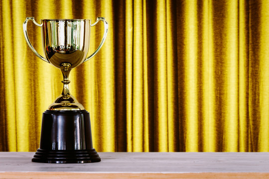 Champion golden trophy on wood table in front of the curtain background