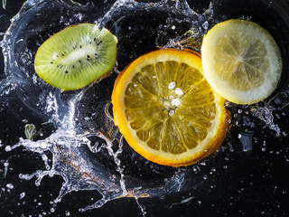 Fototapeta na wymiar Citrus in water on a black background. Splashing water droplets. Kiwi, lemon and orange