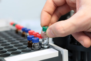 People hand holding a test tube vial sets for analysis in the gas liquid chromatograph. Laboratory assistant inserting laboratory glass bottle in a chromatograph vial