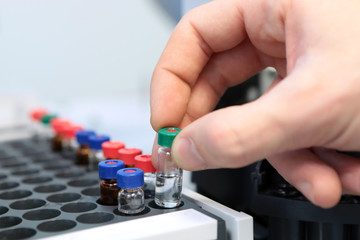 People hand holding a test tube vial sets for analysis in the gas liquid chromatograph. Laboratory assistant inserting laboratory glass bottle in a chromatograph vial