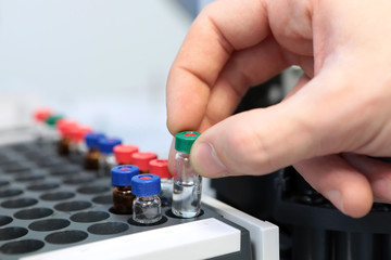 People hand holding a test tube vial sets for analysis in the gas liquid chromatograph. Laboratory assistant inserting laboratory glass bottle in a chromatograph vial