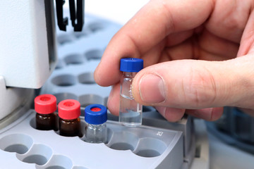People hand holding a test tube vial sets for analysis in the gas liquid chromatograph. Laboratory assistant inserting laboratory glass bottle in a chromatograph vial
