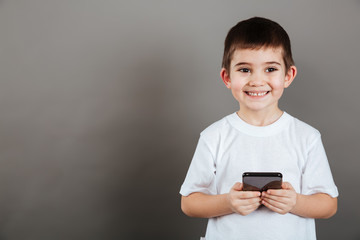 Cheerful little boy standing and using cell phone