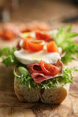 open sandwich with prosciutto, mozzarella and tomatoes on kitchen table, shallow focus