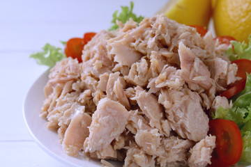 tuna flakes with lettuce, lemon and tomatoes on white wooden table in background.