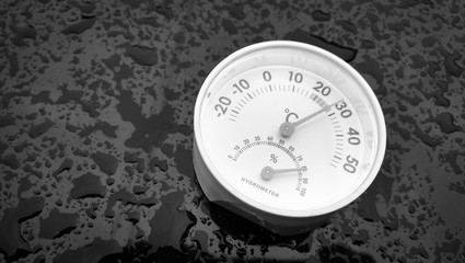 Analog hygrometer putting on a black background filled with drop of water after rain.