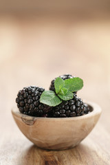 fresh blackberry with mint leaves in wooden bowl on table closeup, with copy space