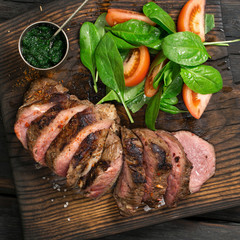 Slices of steak grilled with salad of spinach leaves, tomatoes