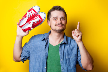handsome young man holding red gumshoes on the wonderful yellow background