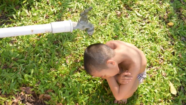 Close up young asian boy taking water from old faucet in the garden. Water shortage and drought concept