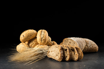 Buns and ciabatta, bread slices on dark wooden table. Barley and fresh mixed breads isolated on black background. Food, bakery concept