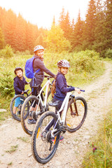 Obraz premium Young girl with her mother and small brother enjoying cycling in forest. Family riding bike concept background