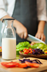 Milk in bottle with woman cooking and vegetables.