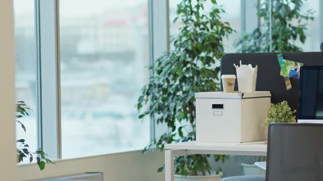 Tracking shot of empty workplace in modern office. Camera moving from window to table with computer, flowerpot and office supplies on it