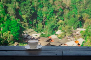 Cup of Hot Cappuccino coffee on wooden table with Rural villages, forests and mountains background . Afternoon Tea and coffee break