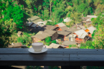 Cup of Hot Cappuccino coffee on wooden table with Rural villages, forests and mountains background . Afternoon Tea and coffee break