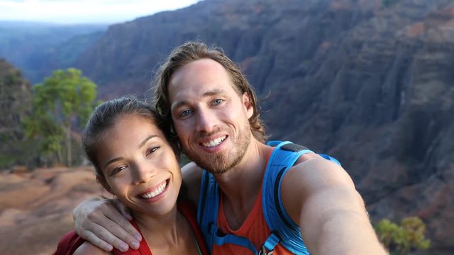 Couple taking selfie video having fun on hike on Hawaii. Woman and man in love taking candid selfportrait while on hiking travel in Waimea Canyon State Park, Kauai, Hawaii, USA.