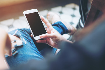 Mockup image of hand holding white mobile phone with blank black screen on leg with a vintage tile...