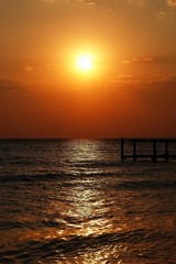 Golden natural sea sunset view of small bridge at horizon and red sky landscape. Sunset reflection in nature with sun in clouds.