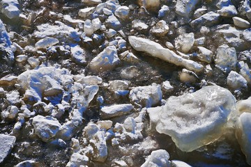 Beautiful natural background. Pieces of ice frozen in the clear river water on a bright Sunny day