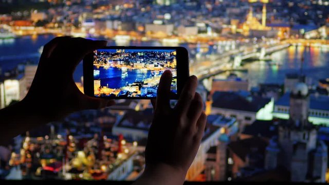 Woman takes a picture of night Istanbul with her smartphone camera. Turkey