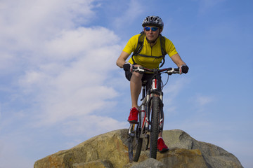 Fototapeta premium Downhill rider, in yellow t-shirt and red sneakers, on mountain bike with cloudy sky background