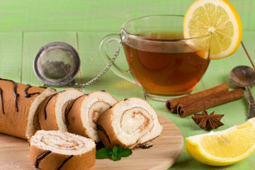 Biscuit swiss roll with a cup of tea on green wooden background