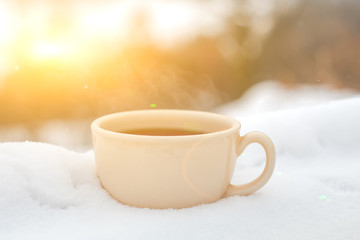 Nice warm cup of tea or coffee outdoors on the snow on a background of a winter landscape. Cozy winter still life.