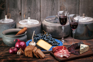 Meat and cheese appetizers selection on a rough old wood background with grapes, two glasses of wine and pottery