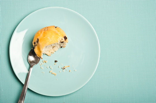 half eaten vanilla maffin with chocolate chips on a plate over aquamarine background with copy space, 