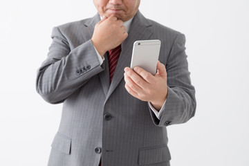 携帯電話を持つビジネスマン、顎に手をつける、困る、中年男性