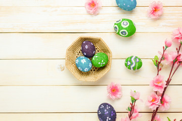 Top view easter background.Happy easter eggs pained on basket also beautiful pink flower.Texture rustic white wooden with decorations and copy space.