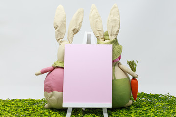 Easter bunnies behind the pink art board and wooden easel on the green grass.