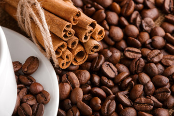 Obraz na płótnie Canvas Coffee beans and cinnamon on a background of burlap. Roasted coffee beans background close up. Coffee beans pile from top with copy space for text. Seasoning. Spice. Cinnamon. Badian. Coffee house.