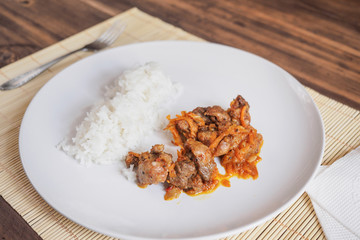 Scene with snow white ceramic dish of rice and roast meat, stew, meats with vegetables on a bamboo napkin on a wooden table from the old boards. Slices of white bread on the white paper napkins