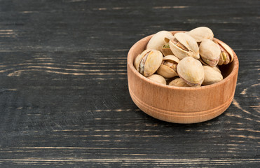 Salted pistachio nuts in a bowl on a wooden background