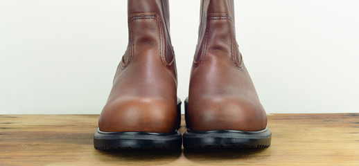 A pair of brown color leather safety boot with white background on wooden surface