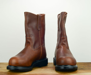 A pair of brown color leather safety boot with white background on a wooden surface