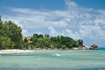 Granite stones on tropical white-sand beach next to turquoise water