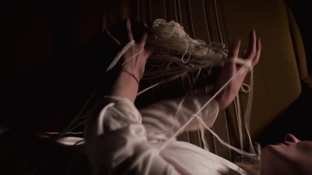 Mentally ill girl lies on a sofa over black background. Her body was tied up threads. She tries to get rid of them
