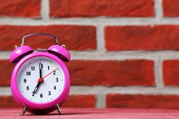 Pink alarm clock on the brick wall background