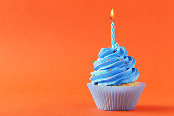 Tasty cupcake with candle on orange background