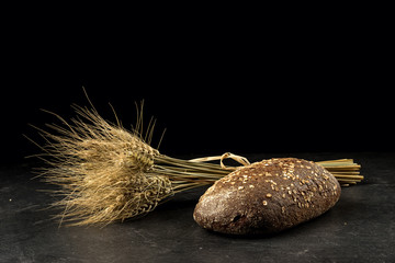 Rye bunch and bread on dark wooden table,  isolated on black background. Food, bakery concept