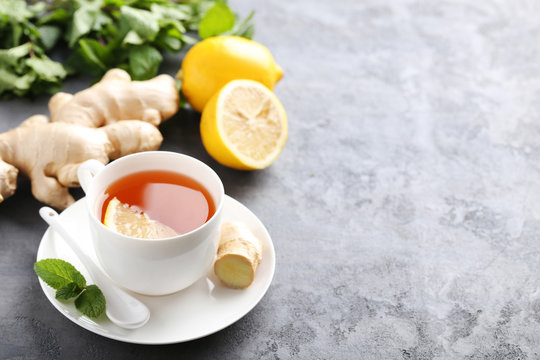 Cup of tea with ginger root and lemon on grey wooden table