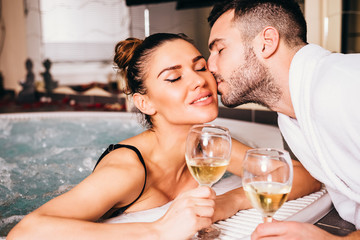 Beautiful young couple relaxing together and drinking white wine in spa