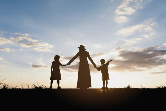 Silhouette of mother and kids holding hands at sunset