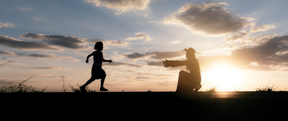 a silhouette of a happy girl child running into the arms of his loving mother for a hug, in the sunset , panoramic banner background